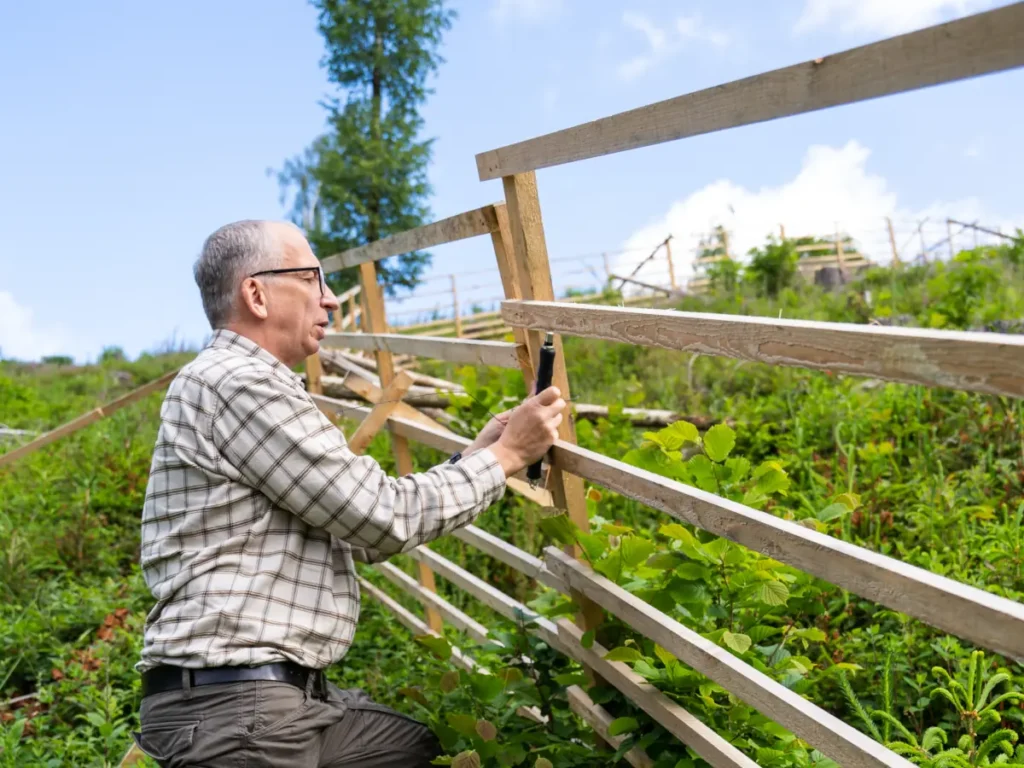 Mann montiert Hordengatter Zaunelement im Wald, flächiger Wildschutz aus Holz